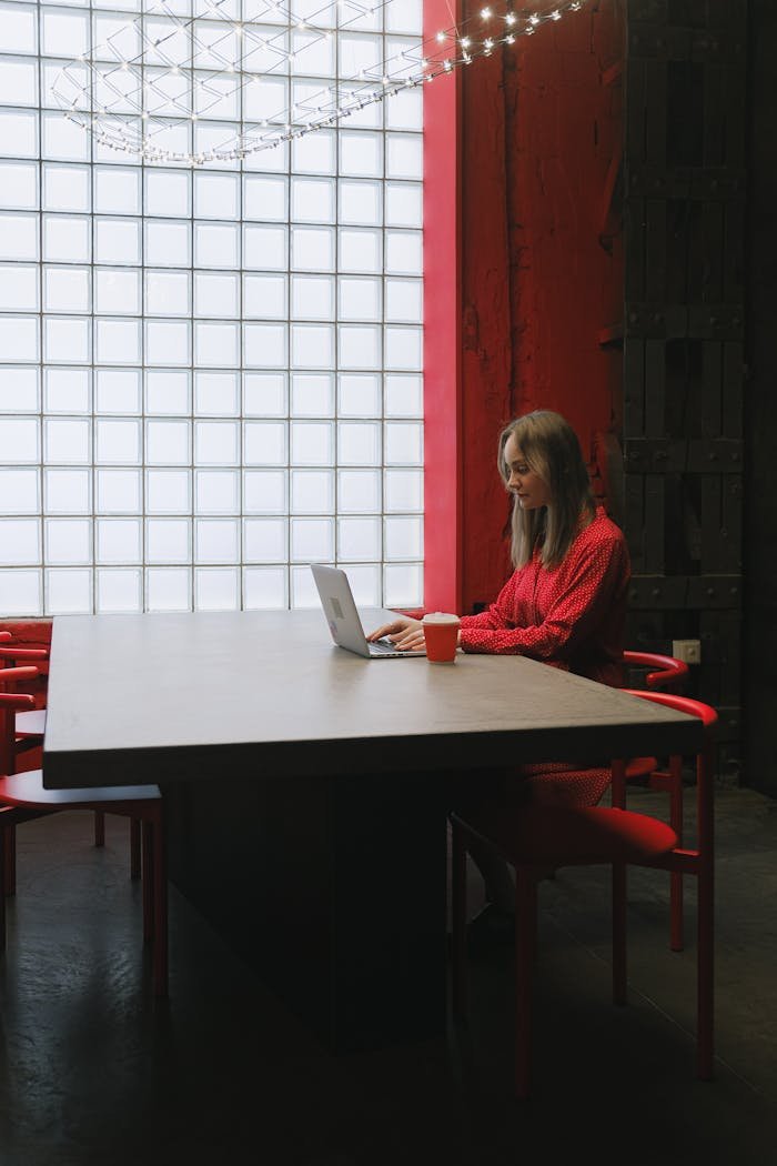 Woman in red sweater working on a laptop in a modern office setting.